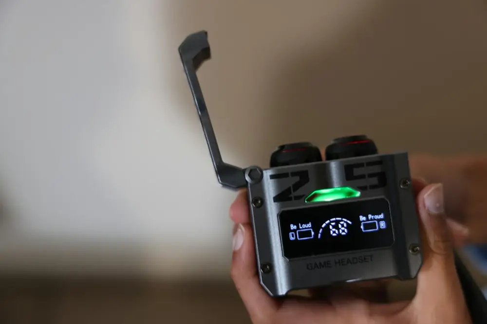 A person holding a grey wireless earbud charging case with a digital display and green light, illustrating narrative